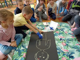 Chłopiec w rękawiczkach przykleja plaster na rysunek z chłopcem. 
