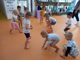 Dzieci przebrane w stroje gimnastyczne schylają się po kolorowe kółka, które układają na środku sali.
