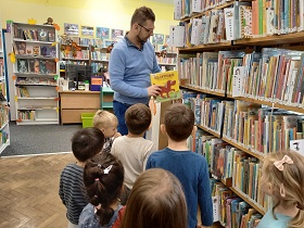 dzieci ustawione są przed Panem, który wkłada na półkę książkę o Cliffordzie.