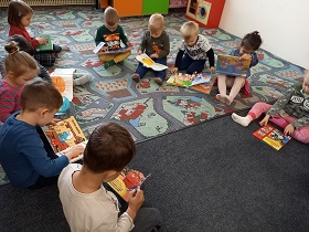 dzieci siedzą na dywanie i oglądają książki.