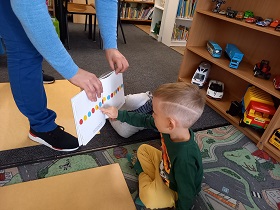 Pan trzyma książkę z narysowanymi kółkami, chłopiec wskazuje palcem na żółte kółko.