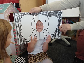 Dziewczynka przykłada twarz do książki. Na ilustracjach widnieje słoń. Książka ma w środku dziurę, przez którą wystaje twarz dziewczynki. 