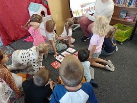 Dzieci siedzą na dywanie i oglądają ilustracje książki. Na dywanie lezą kartoniki z ilustracjami. 