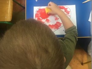 Dziecko maluje serce gąbką, maczając ją w czerwonej farbie.