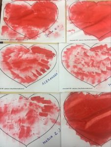 Kartki A4 z sercami pomalowanymi przez dzieci czerwoną farbą za pomocą gąbki.