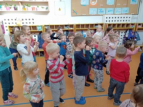 Dzieci stoją ustawione w gromadzie i trzymają ręce zaciśnięte w pięść, udając, że grają na trąbce.