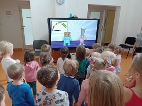 Dzieci stoją w gromadce i wpatrują się w ekran monitora. Na monitorze wyświetlane są postaci Lamy i Krokieta.
