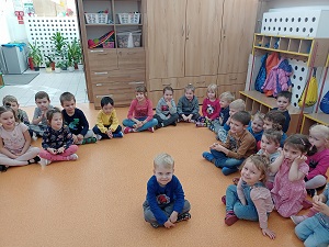 Dzieci siedzą na podłodze w siadzie skrzyżnym z uśmiechami na twarzy.