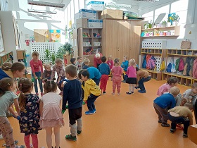 Dzieci stoją w podgrupkach i trzymają w rękach kolorową gumę. Schylają się w stronę podłogi.