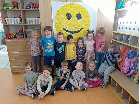 Dzieci stoją przed uśmiechniętą buzią wyklejoną żółtymi i czarnymi kawałkami krepiny.