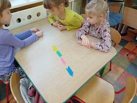 Trzy dziewczynki przy stoliku dzielą patyczki na odpowiednie kolory. 