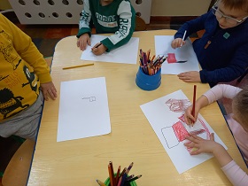 Dzieci siedzą przy stolikach i rysują flagę Polski.
