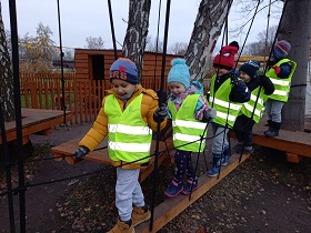 Czworo dzieci przechodzi po drewnianej desce zawieszonej na linach. Na pomoście stoi chłopiec i trzyma się liny.