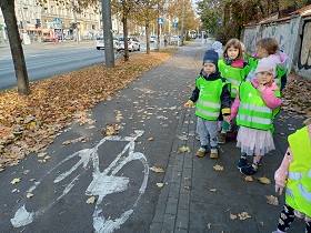Dzieci w zielonych kamizelkach spoglądają na ścieżkę rowerową, na której jest namalowany biały rower.