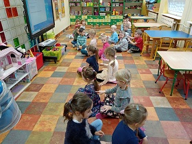 Dzieci siedzą w parach na podłodze. Jedna osoba z pary siedzi do drugiej plecami. Druga osoba palcem ją masuje.
