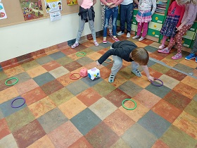 Chłopiec zbiera fioletowe kółko. Na podłodze leżą kółka zielone, czerwone i fioletowe oraz kostka czerwona i biała do gry.