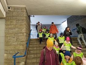Dzieci stojące w parach wraz z dorosłymi schodzą po schodach.