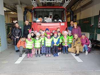 Dzieci wraz z dorosłymi i strażakiem pozują do zdjęcia na tle wozu strażackiego.