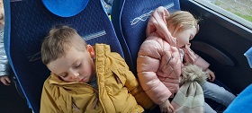 Chłopiec w żółtej kurtce i dziewczynka w różowej kurtce, śpią w autokarze zmęczeni po podróży.