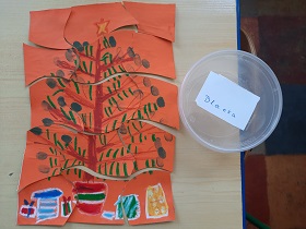 Na stole leżą ułożone puzzle. Na pomarańczowym obrazku jest choinka z kolorowymi bombkami, pod nią leżą prezenty w kolorowych opakowaniach.