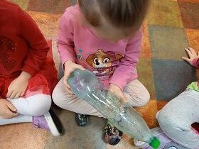 Dziewczynka siedzi i ogląda butelkę w której widać lód.