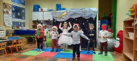 Ośmioro dzieci ubranych świątecznie, tańczą i śpiewają.