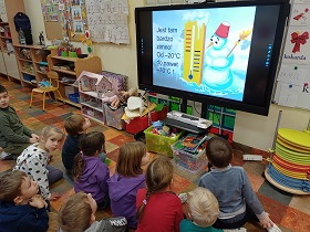 Dzieci siedzą na podłodze przed monitorem. Na monitorze wyświetlany jest bałwan z termometrem.