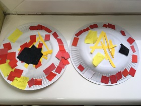 Dwa papierowe talerze, wyklejone są czerwonymi i czarnymi kwadracikami z papieru oraz żółtymi paskami.