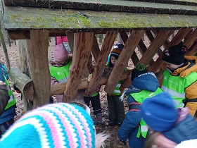 Dzieci w zielonych, odblaskowych kamizelkach stoją przy paśniku dla zwierząt.