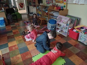 Dzieci pracują w parach na podłodze. Jedna osoba z pary leży na macie, druga siedzi przy niej. i ją masuje. 