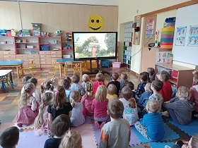 Dzieci siedzą na podłodze przed monitorem, na którym wyświetlany jest film. 