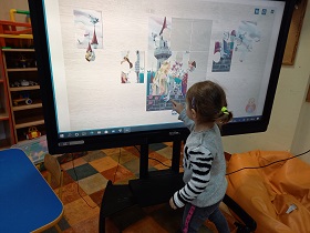 Przed monitorem stoi dziewczynka i układa puzzle – zamek.
