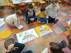 Dzieci siedzą na kolorowych poduszkach i spoglądają na plansze z piramidami zdrowia. 