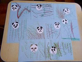 Na stoliku leżą prace plastyczne dzieci. Są to przyklejone pandy na niebieskiej kartce z dorysowanymi gałązkami bambusowymi.