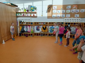 Dzieci w strojach gimnastycznych stoją w kolejce by strzelić chłopcu, który stoi przy szafie, bramkę. 