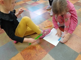 Dwie dziewczynki mierzą linijkami swoje stopy. 