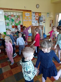 W sali dzieci stoją i wyginają się w różne kierunki. 