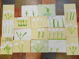 Na podłodze znajdują się prace dzieci. Przedstawiają białe kwiatki z zielonymi łodygami i listkami.