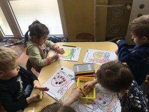 4 dzieci koloruje rysunek konturowy ślimaka i wykleja go kółeczkami w różnych kolorach