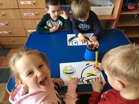 Dziewczynka i 3 chłopców kolorują plakat kredkami.
