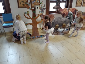 Cztery dziewczynki i chłopiec znajdują się przy makietach drzewa oraz zwierząt. Jedna z nich klęczy pod drzewem. 