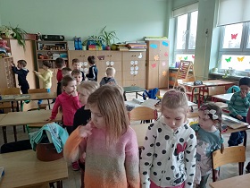 Dzieci znajdują się w sali klasowej między stolikami. 