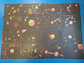 Prace plastyczne dzieci ułożone na niebieskim tle. Są to kolorowe układy słoneczne wydrapane na czarnych kartkach. 