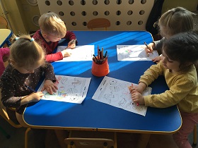 Czwórka dzieci siedzi przy stoliku i koloruje symbole związane z Wielkanocą.