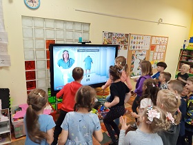  Dzieci skaczą przed ekranem na którym ukazana jest postać skaczącego mężczyzny na niebieskim tle. Na dole ekranu znajduje się napis hop.