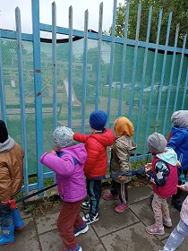 Dzieci patrzą na swój plac zabaw przez ogrodzenie.