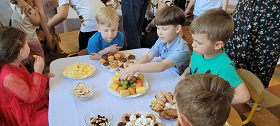 Piątka dzieci siedzi przy stoliku i je owoce i ciastka ze stolika.