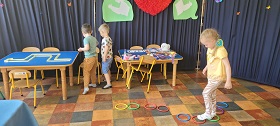 Dziewczynka przechodzi stawiając stopy w kółko. Dwóch chłopców stoi przed stołem na którym ułożony jest labirynt.