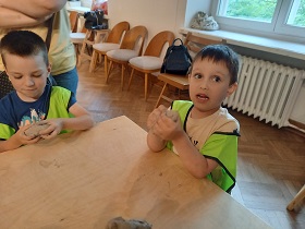 Przy stole stoją dwaj chłopcy którzy gniotą w dłoniach glinę.