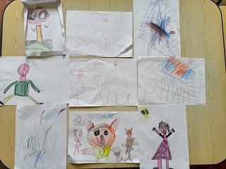 Na stole ułożone są prace dzieci przedstawiające ich przyjaciół. 